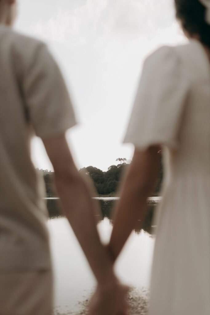 Blurred view of a couple holding hands by a serene lake, evoking romance and tranquility.