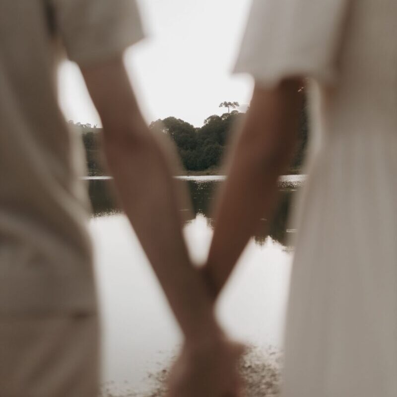 Blurred view of a couple holding hands by a serene lake, evoking romance and tranquility.