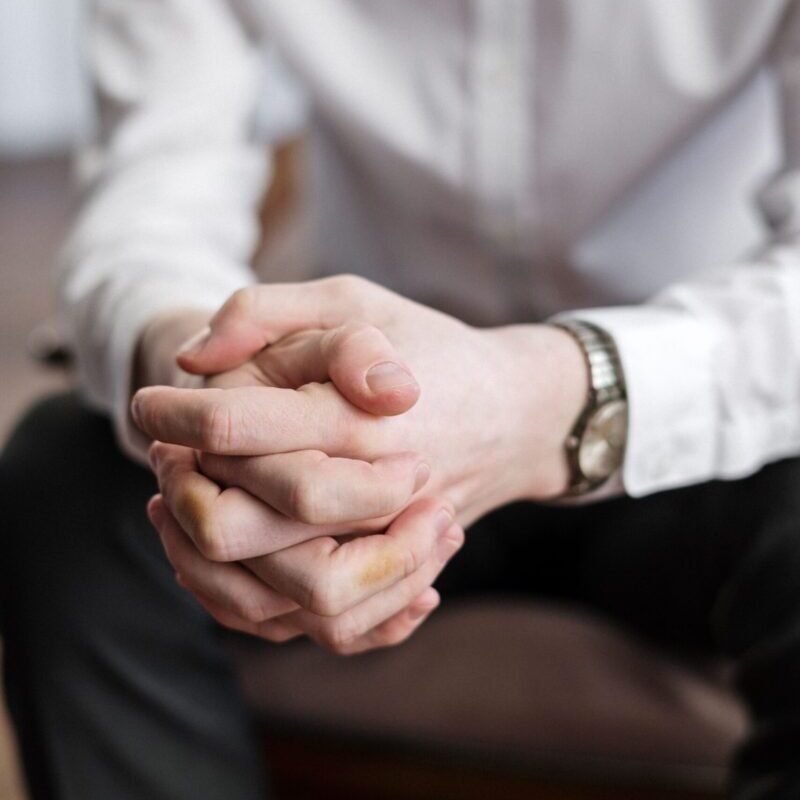 Close-up of a man's hands clasped in an indoor setting, signifying contemplation.
